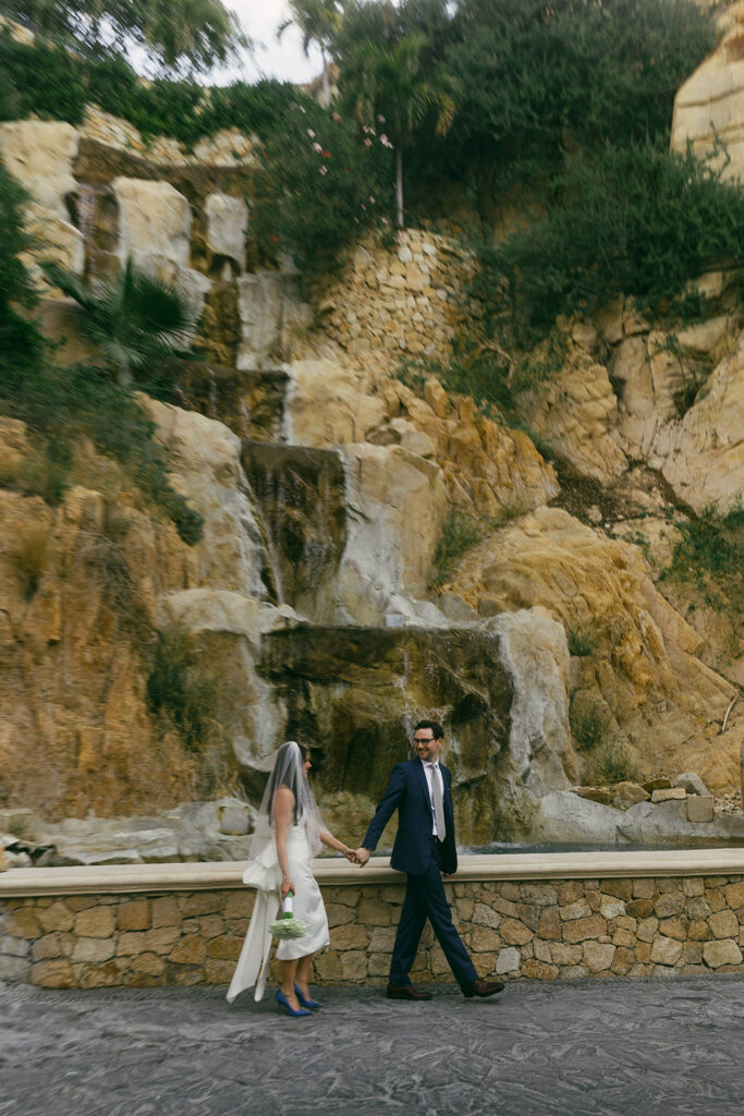 couple walks holding hands by waterfall