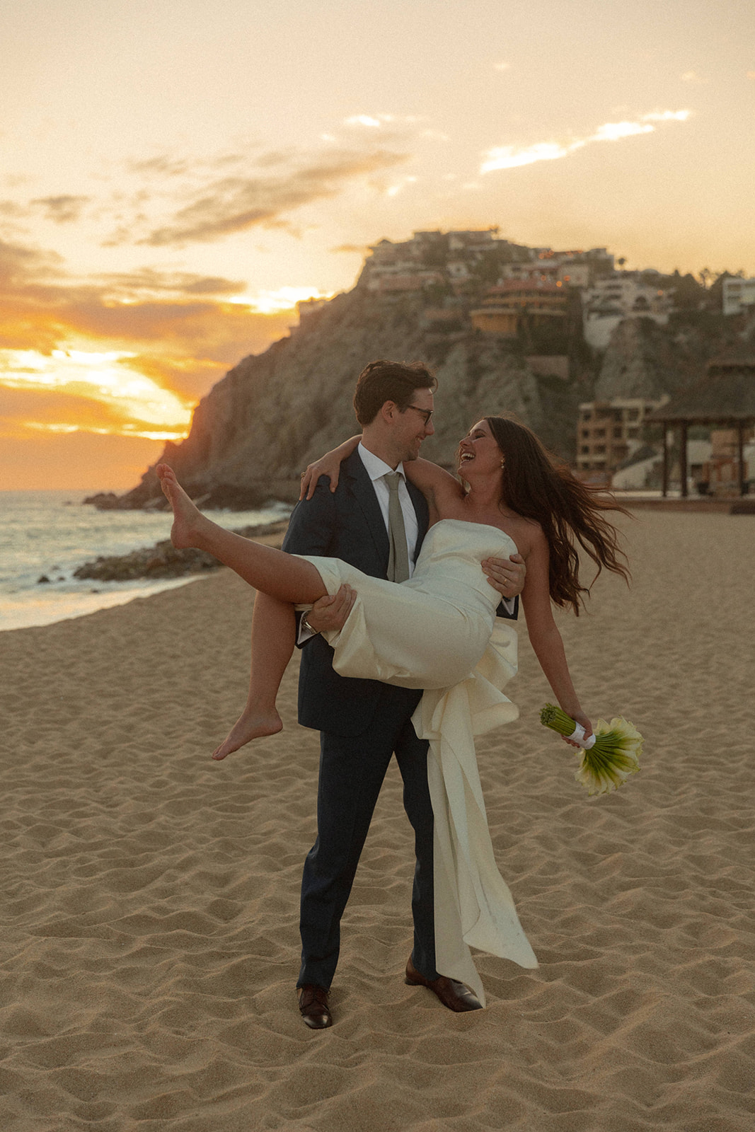 groom carries bride at sunset beach elopement