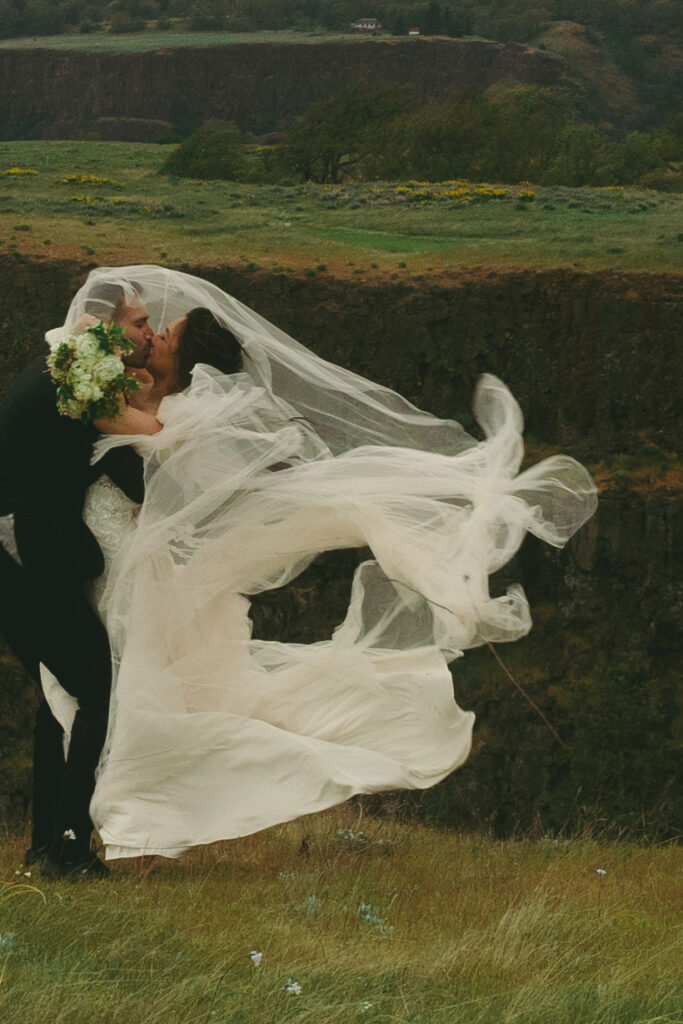 couple kisses with wedding dress flowing in the wind at outdoor elopement