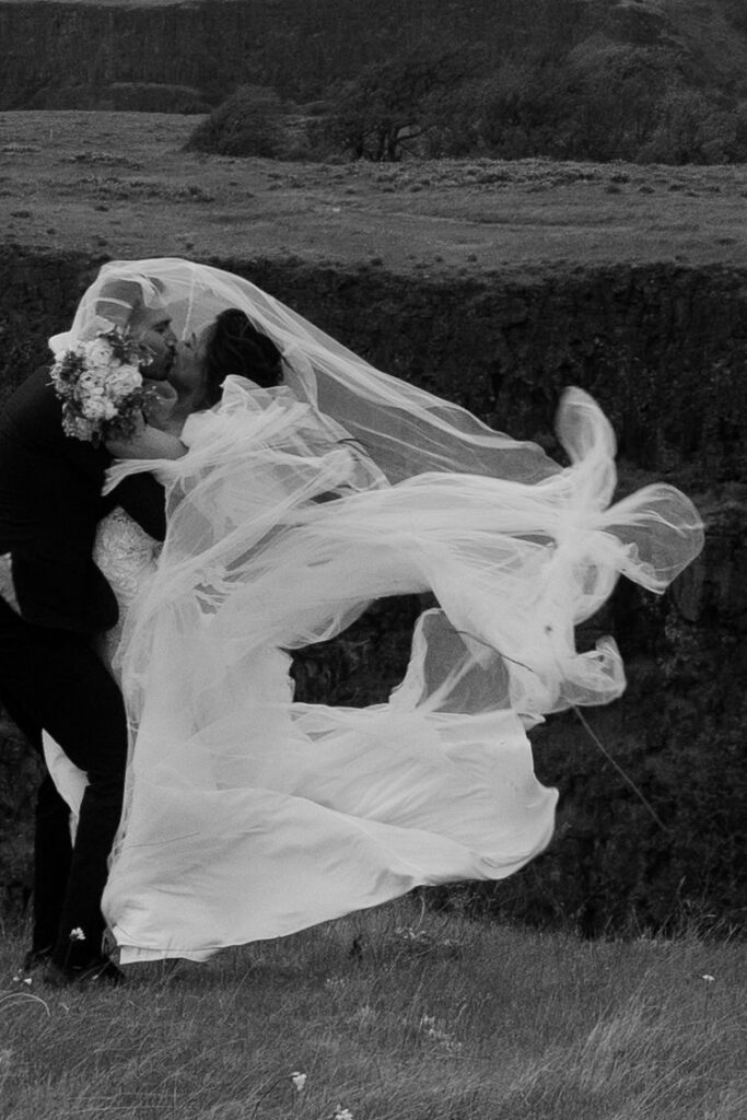 couple embraces with wedding dress flowing in the wind at outdoor elopement