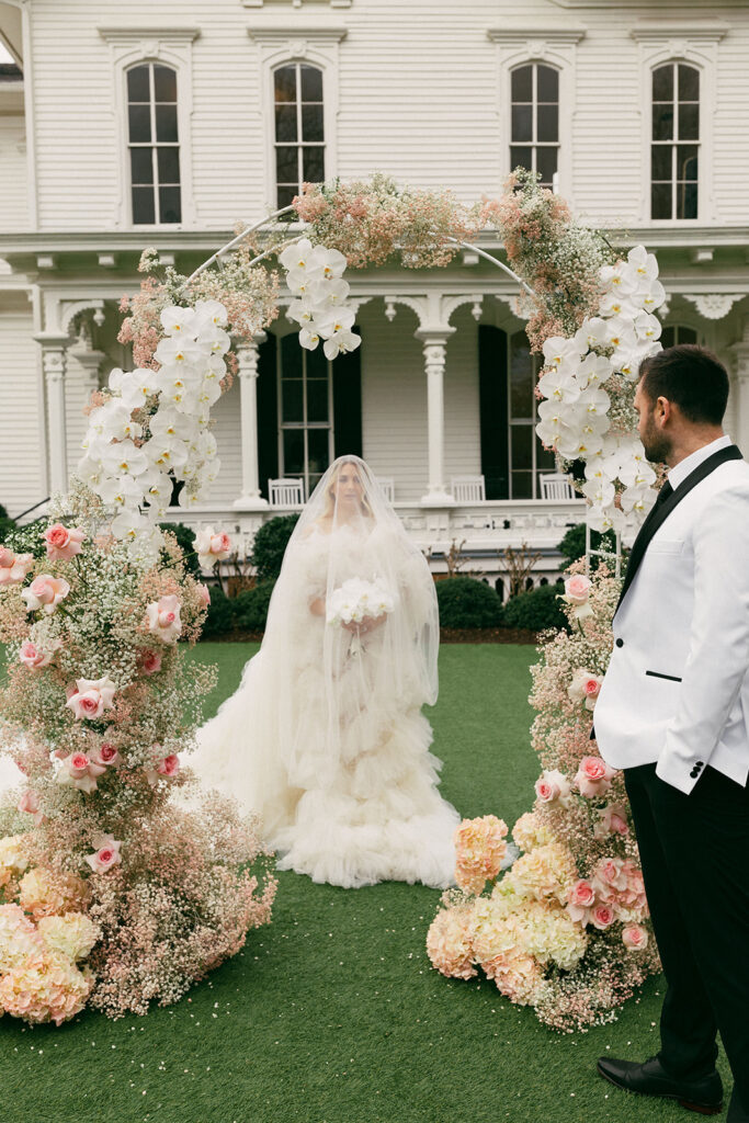 couple stands under flower arch at backyard wedding