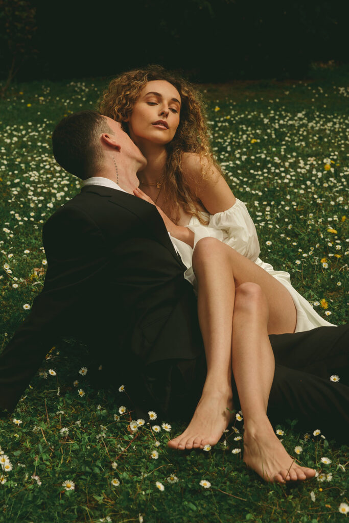 bride sits in groom's lap in flowery field