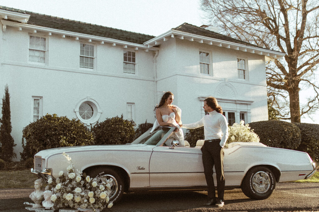 couple stands with white vintage car at Raleigh North Carolina wedding venues