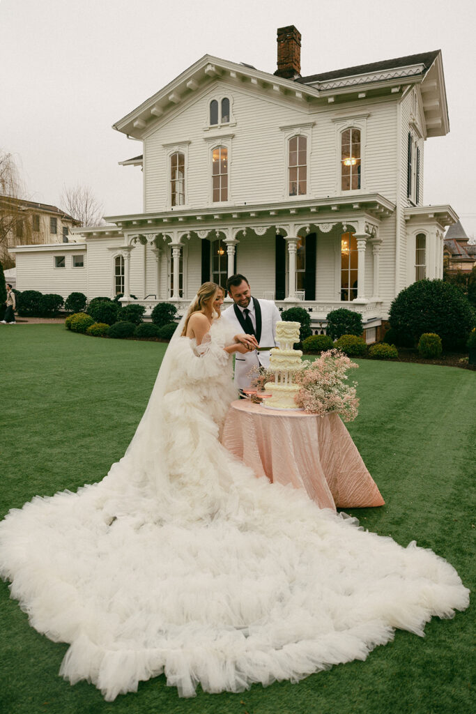 couple cuts cake on lawn beside wedding venue estate