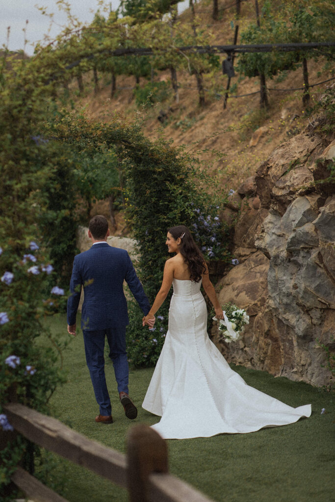 couple walks holding hands through garden at Malibu wedding 