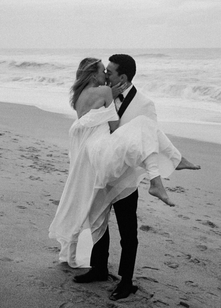 groom carries bride kissing at beach elopement