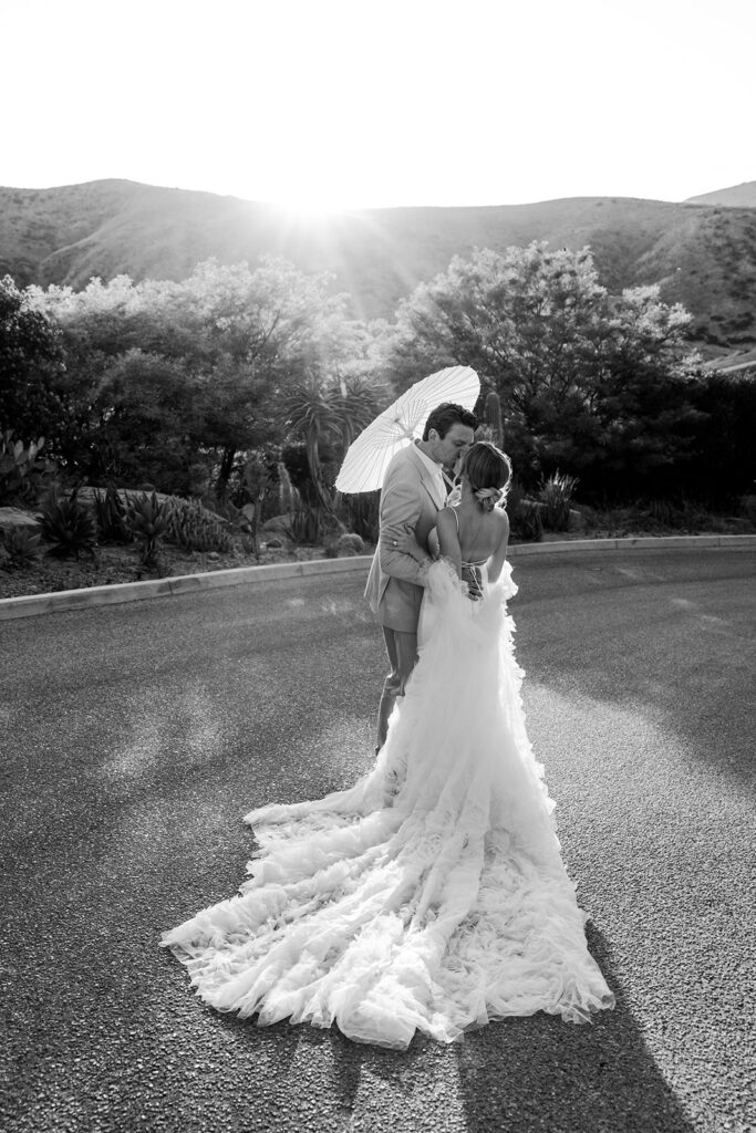 couple walks at sunset outdoor wedding holding parasol