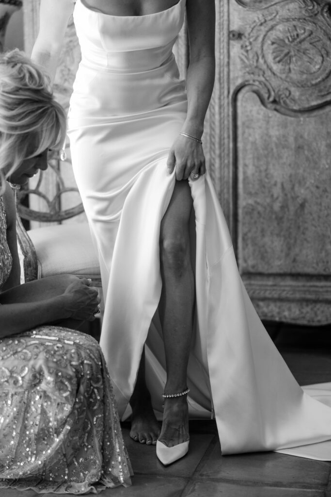 bride holds up dress putting on wedding shoes