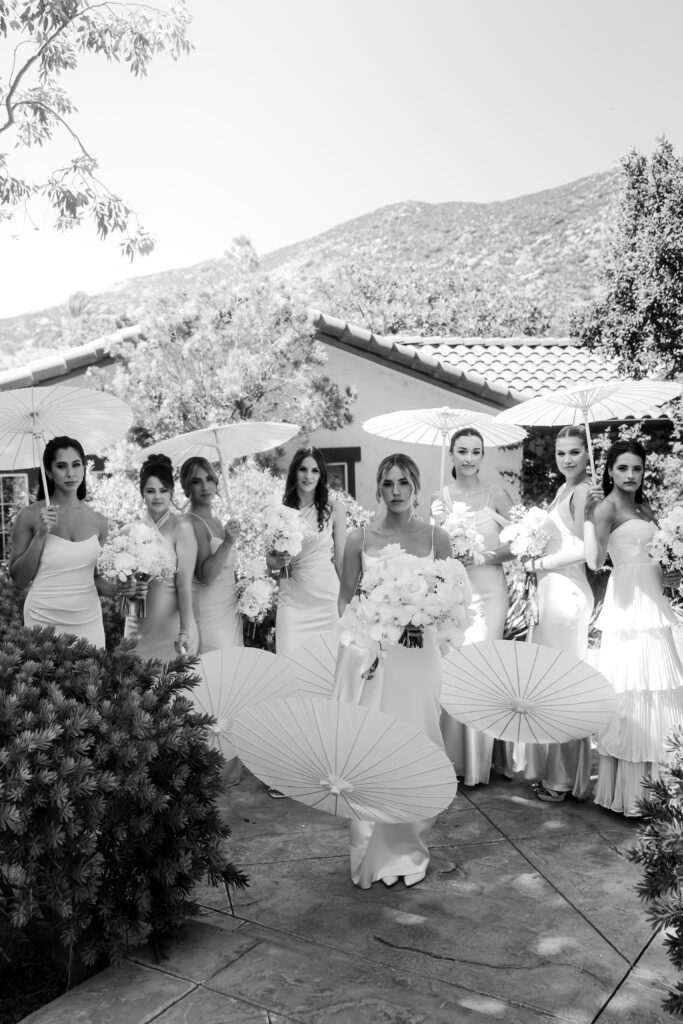bride stands with bridesmaids holding white parasols