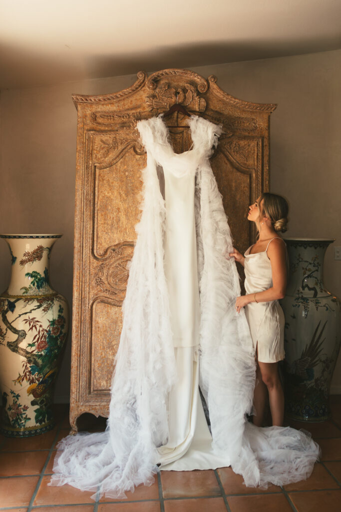 bride stands beside wedding dress and veil on wardrobe