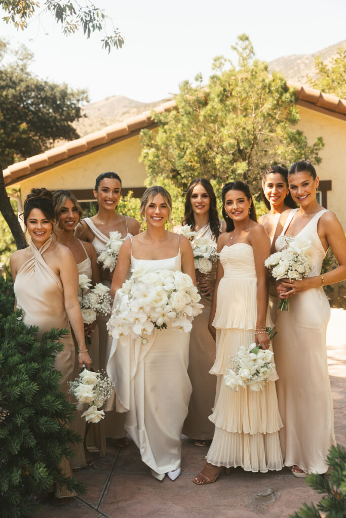 bride stands with bridesmaids holding white parasols