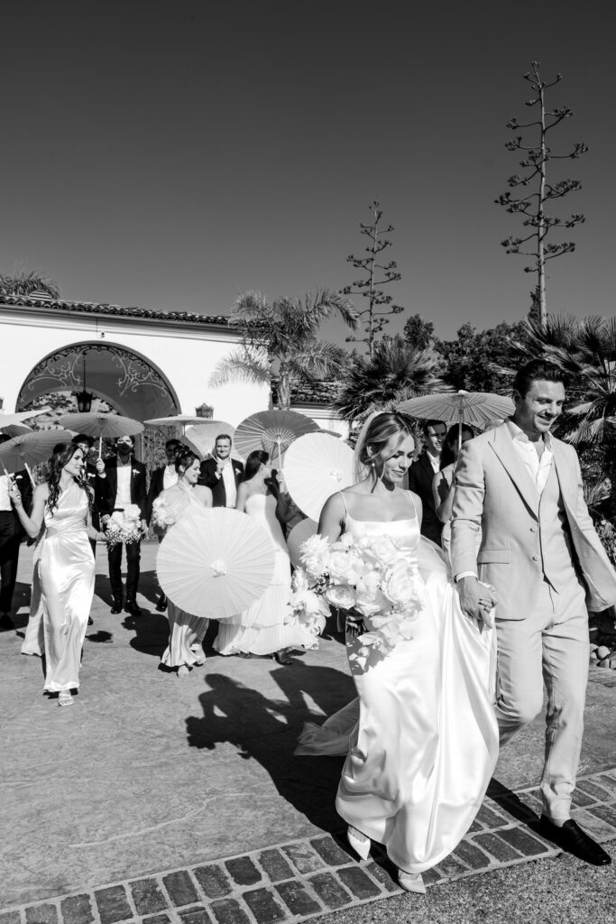 couple walks with wedding party holding parasols