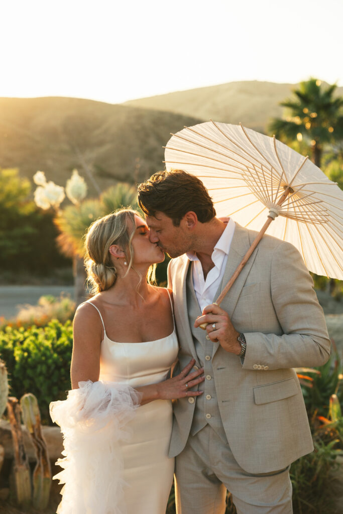 couple kisses holding wedding parasol