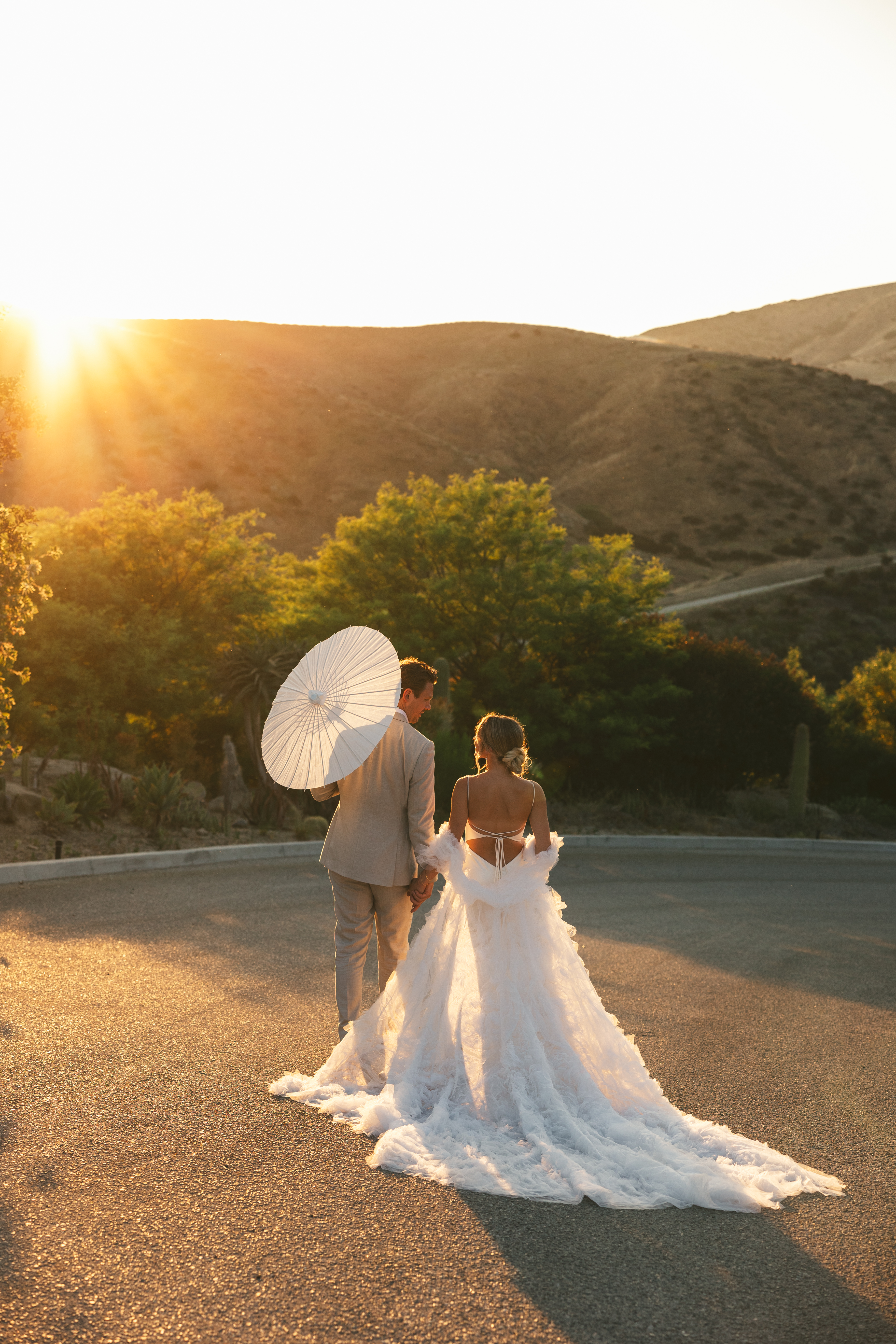 couple walks with parasols at sunset summer wedding