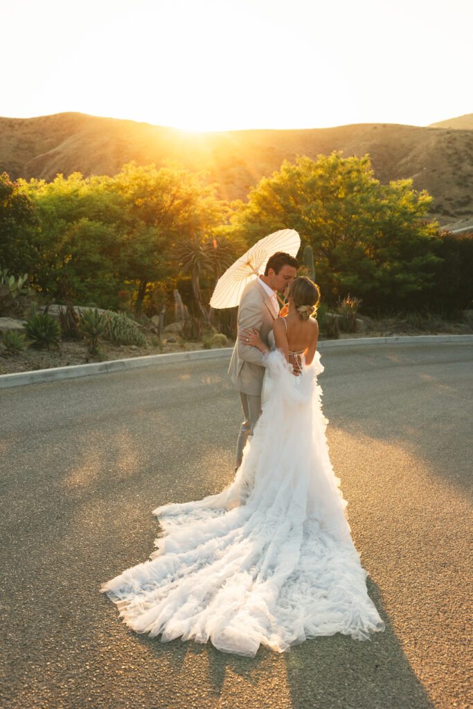 bride and groom holding a parasol at sunset