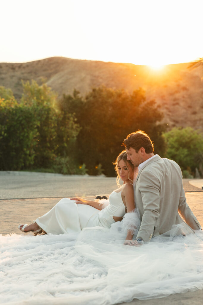 couple sits together on wedding cape at sunset summer wedding