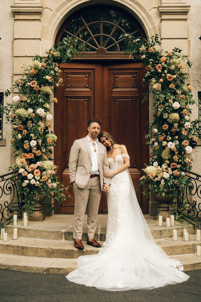 bride embraces on doorstep surrounded by floral arch