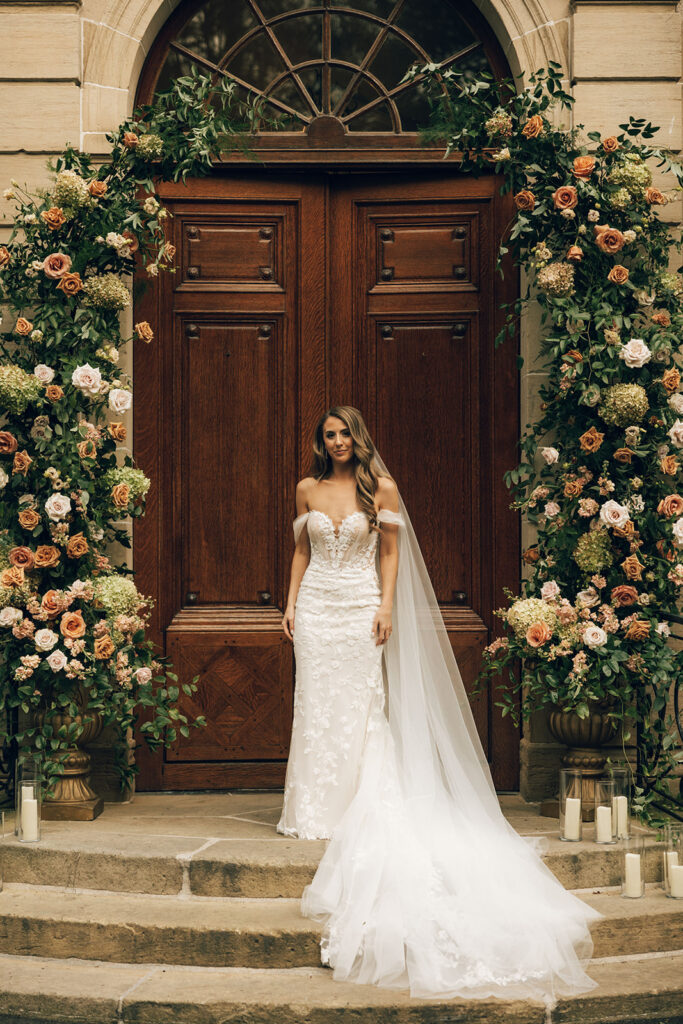 bride stands under wedding floral arch