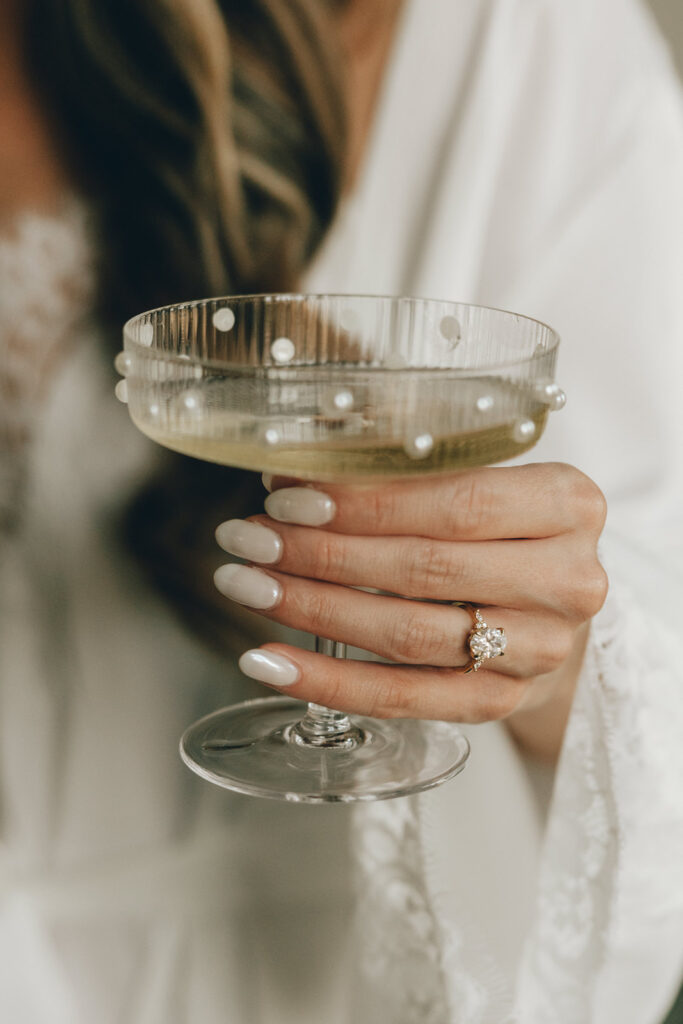 bride with engagement ring holds champagne glass