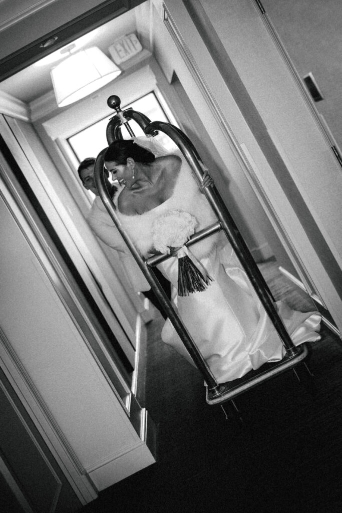 groom pushing bride on elevator luggage cart at hotel down the hall