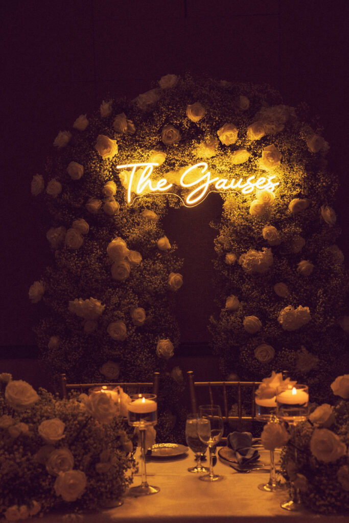 bride and groom's sweetheart table with neon sign and white florals