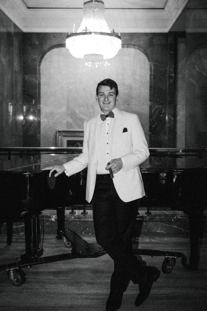 groom with cigar in hand in front of grand piano on wedding day