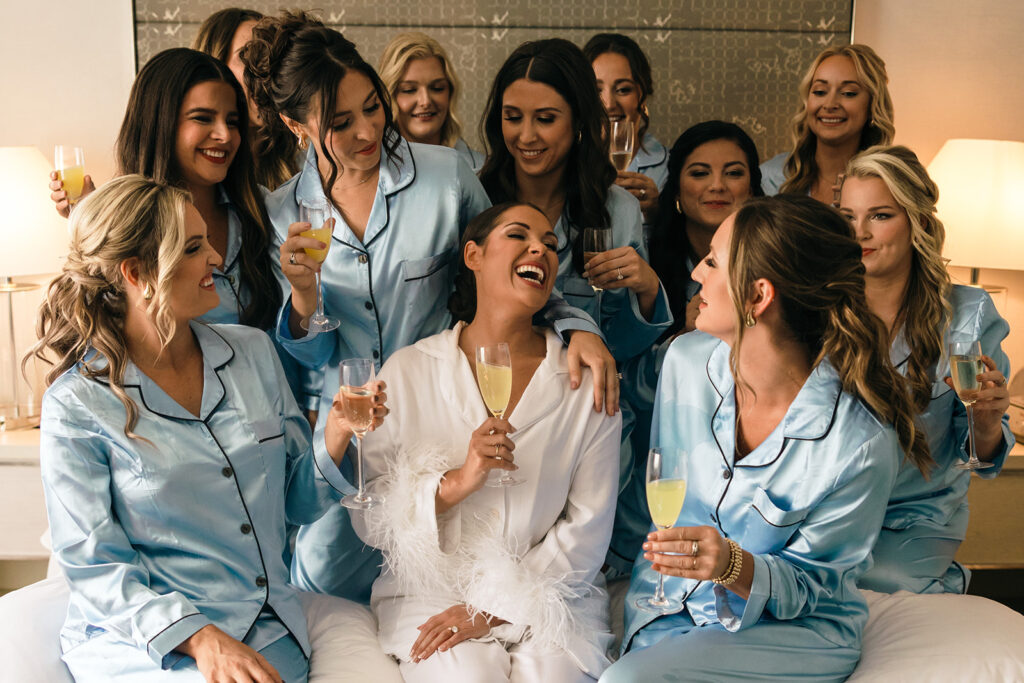 bride laughs with bridesmaids on bed at hotel wedding venue