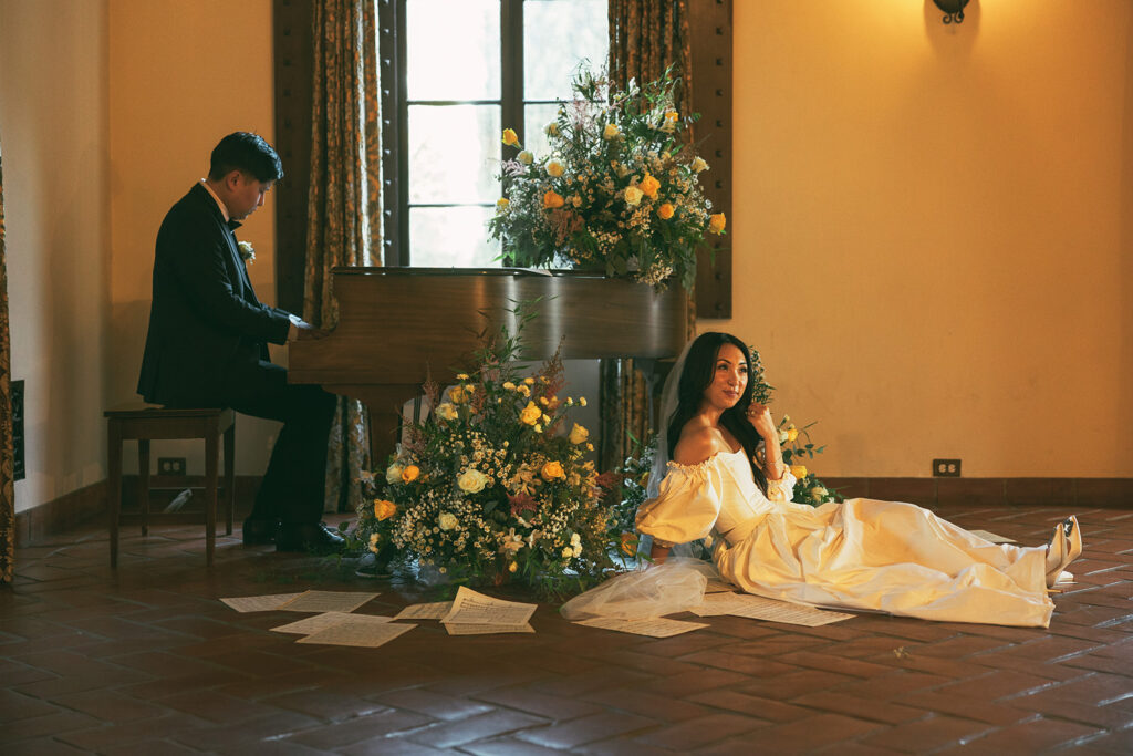 groom plays piano while groom sits by flowers