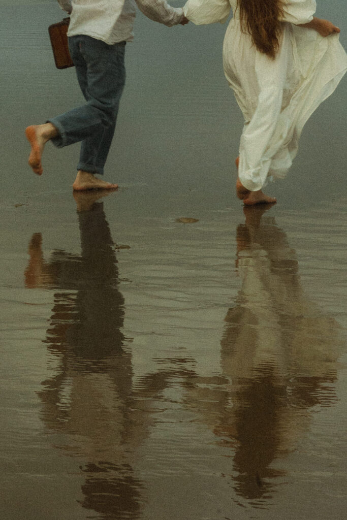 couple holds hands running on Cannon Beach at engagement session
