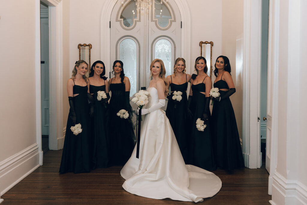 bride poses with bridesmaids holding white rose bouquets 