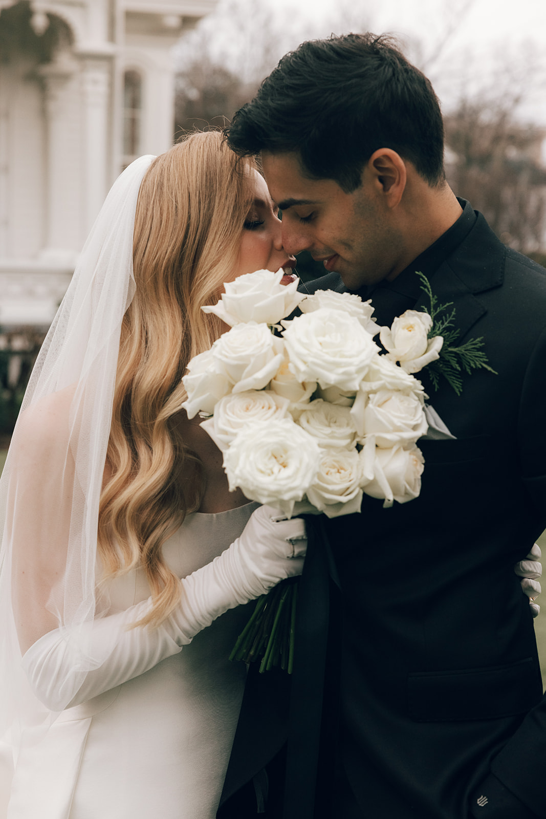 couple kisses behind white rose wedding bouquet