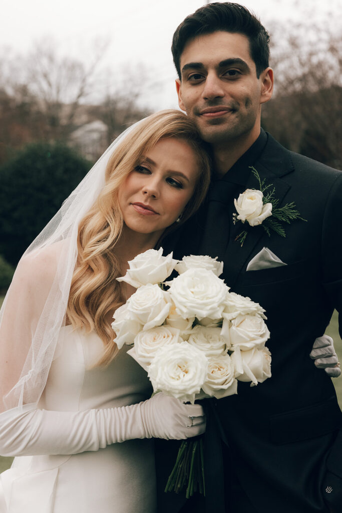 couple embraces holding white rose wedding bouquet 