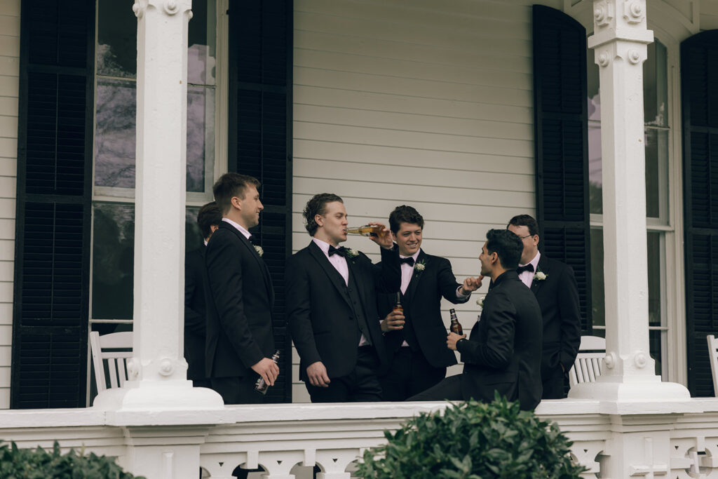 groomsmen drink together on front porch at The Merrimon-Wynne House