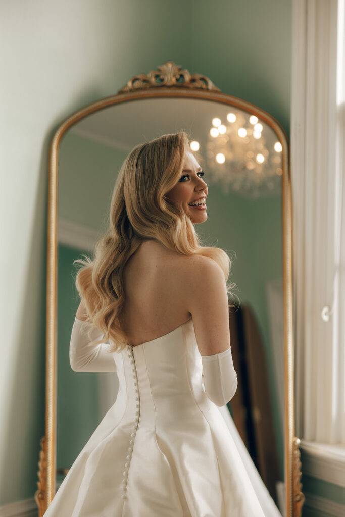 bride stands in front of grand gold mirror 