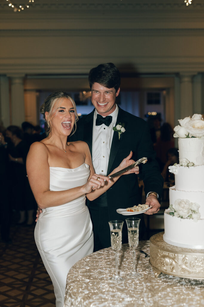 couple laughs while cutting wedding cake 